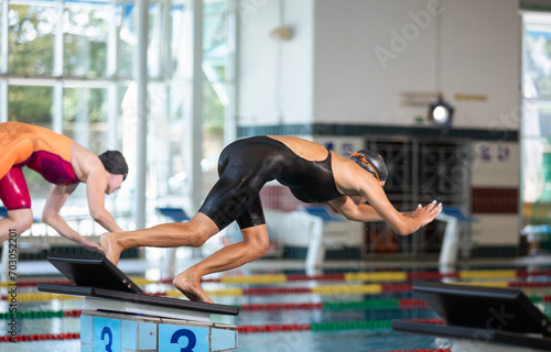 Two professional female swimmers taking track start position on the platform gracefully jumping and diving in a swimming pool. Sport competition concept.