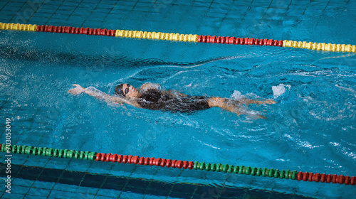 Female athlete in action, performing the backstroke swim technique in the indoor lap pool. Competitive back crawl stroke concept.