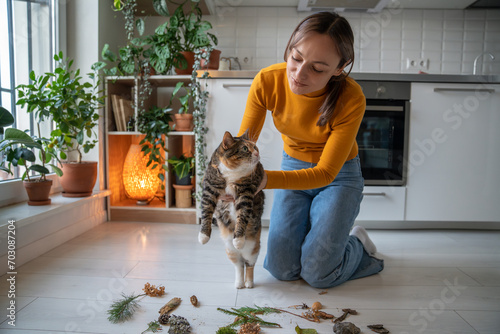 Tender caring pet owner showing to lazy uninterested cat natural objects, twigs brought from park, encouraging energy, interest, activity. Idle cat dreaming of lying, sleeping, resting, doing nothing