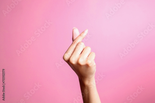 Female hand gesturing showing heart from fingers, korean love symbol over pink background