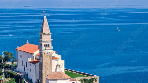 Red rooftop and Saint George Church with panoramic aerial view of coastal town Piran, Primorska, Slovenia, Europe. Shimmering azure waters of Adriatic Sea. Tranquil Mediterranean atmosphere