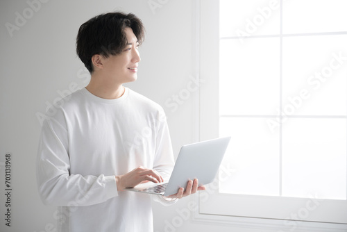 窓際でパソコンを使うハンサムな男性 フリーランス・エンジニア・デザイナーなどのイメージ