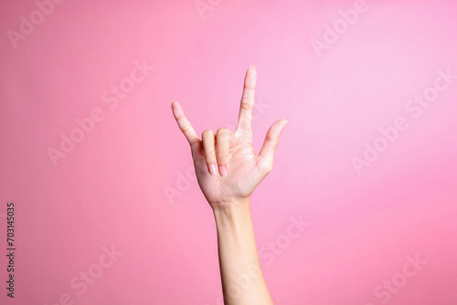 Hand showing rock sign with fingers gesture against pink background, human hand gesture