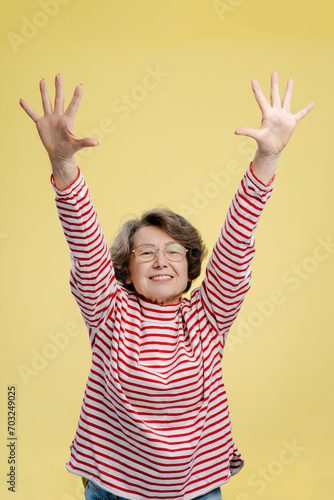 Smiling senior woman, pensioner wearing eyeglasses and stylish casual sweater holding hands up