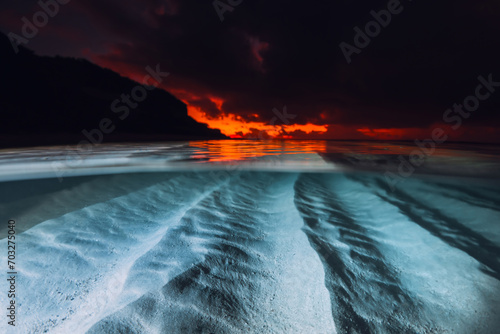 Split view with sunset or sunrise and underwater sandy sea bottom. Tropical sea with bright sunset or sunrise, underwater view with flash light