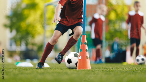 Youth in sports training. Player kicking ball during a soccer training drill. Slalom practice for football players. Summer sports practice camp for school kids