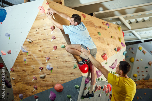 Man in his 30s practicing bouldering activity, climbing on artificial rocks on climbing wall indoors. Training with instructor. Concept of sport, hobby, active lifestyle, school, training course