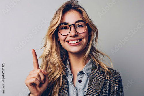 Cheerful young woman with glasses pointing upwards with one finger