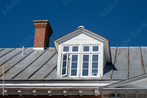 A red brick chimney and a dormer window in an old metal roof