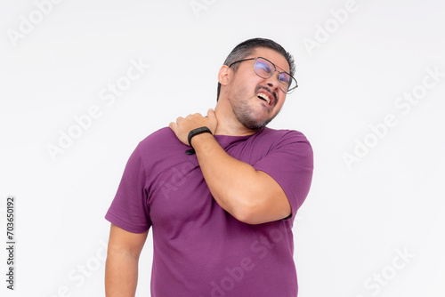 A middle aged man grimaces in pain over sore trapezius muscles. Pulling a muscle or DOMS the next day after a workout. Isolated on a white background.