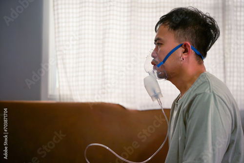 Asian boy wearing oxygen mask. man using asthma inhaler while sitting at home due to allergy. Asia man using spray asthma. 