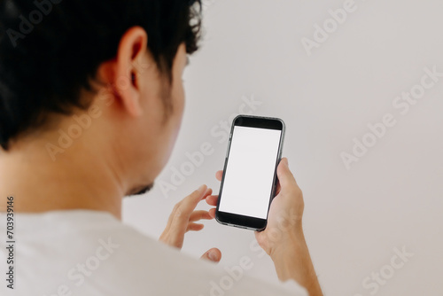 Back side view of Asian man using mobile phone, showing white screen display, isolated on white background wall.