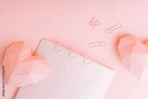 Paper pink hearts with notepad and paper clips on pink background