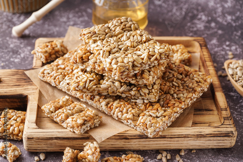 Board with tasty kozinaki, sunflower seeds and jar of honey on grunge grey background