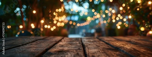 Empty Wood table top with decorative outdoor string lights hanging on tree in the garden at night time. 