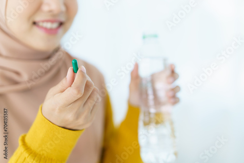 Asian young muslim woman showing a pill and water bottle, muslim woman taking a pill capsule.