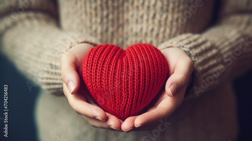 Close-up of a woman in a warm sweater holding a knitted red heart in her hands. Valentine's Day greeting card. A symbol of love.