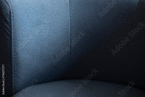 The back of a soft sofa made of a blue shade of fleecy velor stitched with a stitching of thread and a close-up part for sitting with an empty space for text. Armchair in soft fabric and shades.