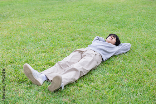 A young man lies down on a green lawn in an outdoor park on a sunny day and relaxes