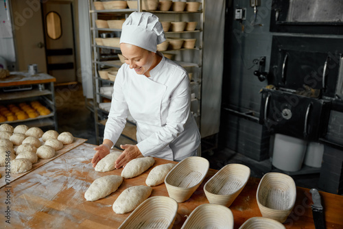 Professional positive woman baker forming loaf from raw dough