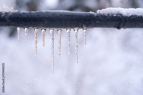 Frozen icicles on a gray pipe after a thaw in winter. Background. Form.