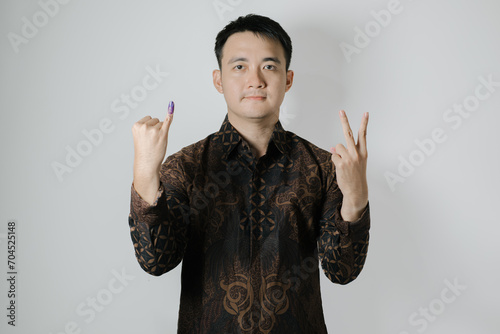 Asian man wearing Indonesian traditional Batik cloth is showing his little finger with purple ink applied to choose number two after Pemilu or Indonesian presidential election on white background
