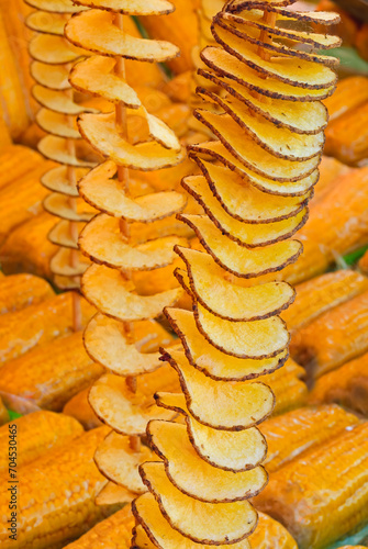 skewers of fried potato chips with peel and yellow organic corn cobs with for sale in street food stall