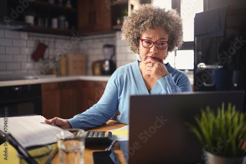 A mature entrepreneur woman of mixed race working on a computer at home. Woman small business owner. Woman working on a computer, calculating monthly expenses, mortgage payments, doing home budgeting