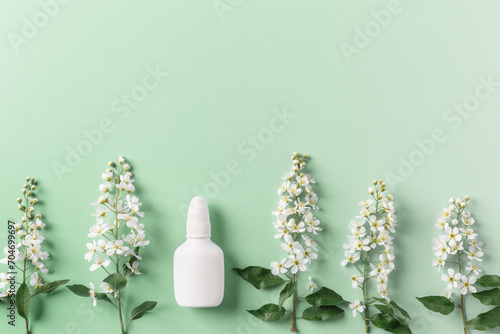 Seasonal spring allergies, fresh spring blooming branches tree and mock up white nasal spray bottle on green background, top view, minimal flat lay style. Seasonal allergy treatment concept.