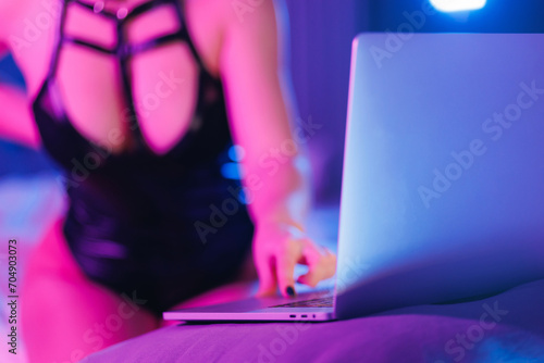 Concept virtual sex, neon light. Internet web cam model beautiful woman working online with laptop.