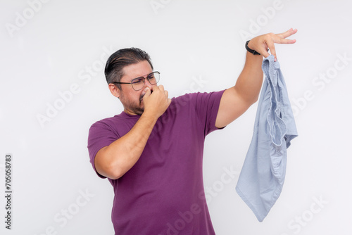 A disgusted middle aged man covers his nose while holding a stinky and smelly pair of boxer shorts with his hand. Isolated on a white background.