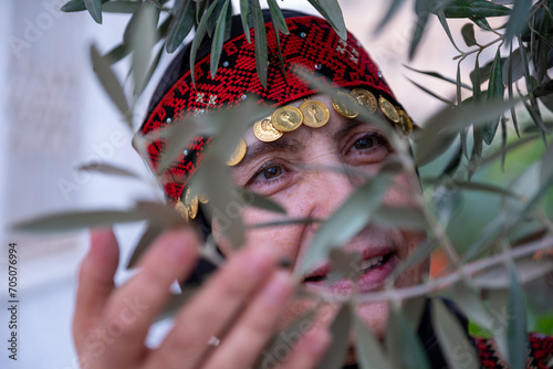 Portrait Of woman wearing palestinian traditional clothes in olive trees field holding branch in her hand