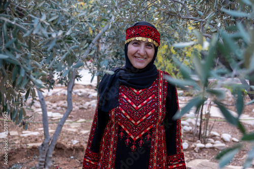 Portrait Of woman wearing palestinian traditional clothes in olive trees field holding branch in her hand