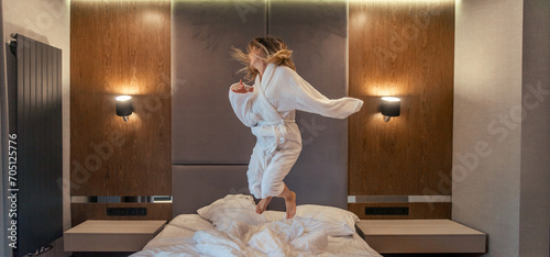 Woman having fun and jumping with bathrobe on bed in hotel room