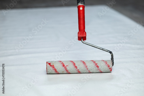 A white paint roller with a red handle. Applying glue to wallpaper