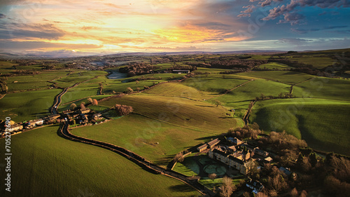 Aerial view of a picturesque rural landscape at sunset with rolling hills, a winding road, and a small village.