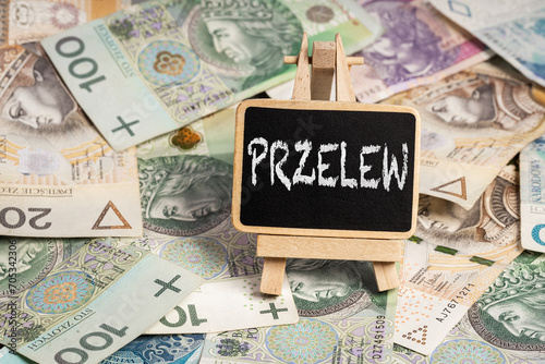 Black writing board on a wooden frame with the inscription "przelew", Polish zloty PLN banknotes scattered in the background (selective focus) translation: transfer