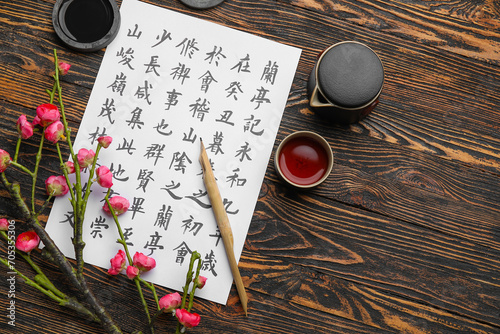 Paper sheet with Asian hieroglyphs, nib pen, ink, cup of tea and blooming branch on wooden background. International Haiku Poetry Day