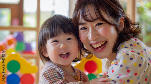 日本の幼稚園児と先生/親子がカラフルなおもちゃで笑顔で遊んでいる写真、背景保育ルーム、木育/幼児教育