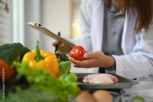 Professional nutritionist in white coat working at desk with vegetables. Healthcare and diet concept