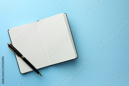 Open notebook with blank pages and pen on light blue background, top view. Space for text