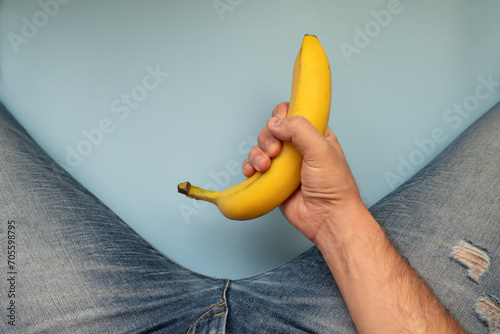 yellow big banana and men's legs in jeans on a blue background. The concept of men's health