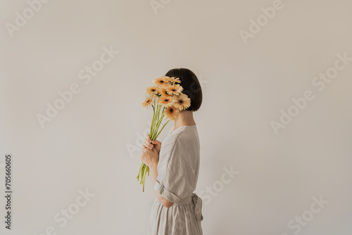Gerbera flowers bouquet in female hands. Young pretty woman in neutral tan sandy beige linen dress