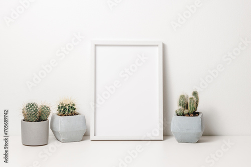 Picture frame mockup with cactus plants in ceramic pots on the white wooden table. Wooden white photo frame with copy space for design, scandinavian cozy home interior
