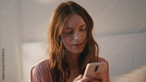 Girl texting mobile phone in bed closeup. Smiling young woman typing smartphone