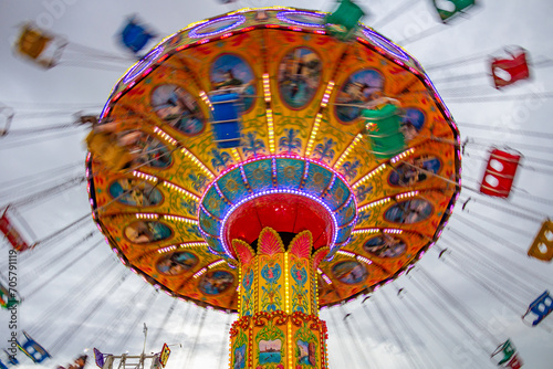 Um brinquedo grande e colorido no parque de diversões com poucas pessoas, em um dia nublado. Foto feita de baixo para cima.