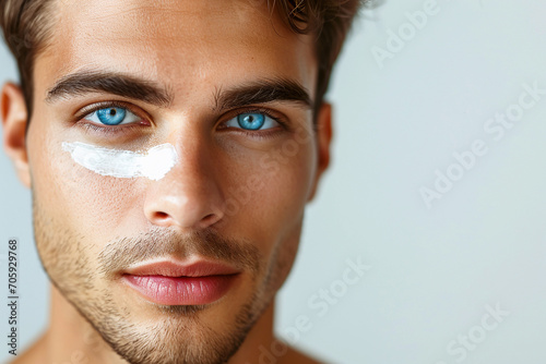 handsome young man with blue eyes has an anti-aging cream under his eye, skin care treatment