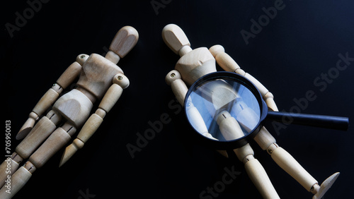 Wooden mannequins and a magnifying glass on a dark background. The theme of gender identity and self-identity. Study of human anatomy. Photo