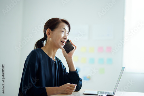オフィスにてスマートフォンで電話をする日本人シニア女性