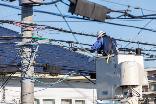 住宅街で電柱の上の電線の修理をする作業員